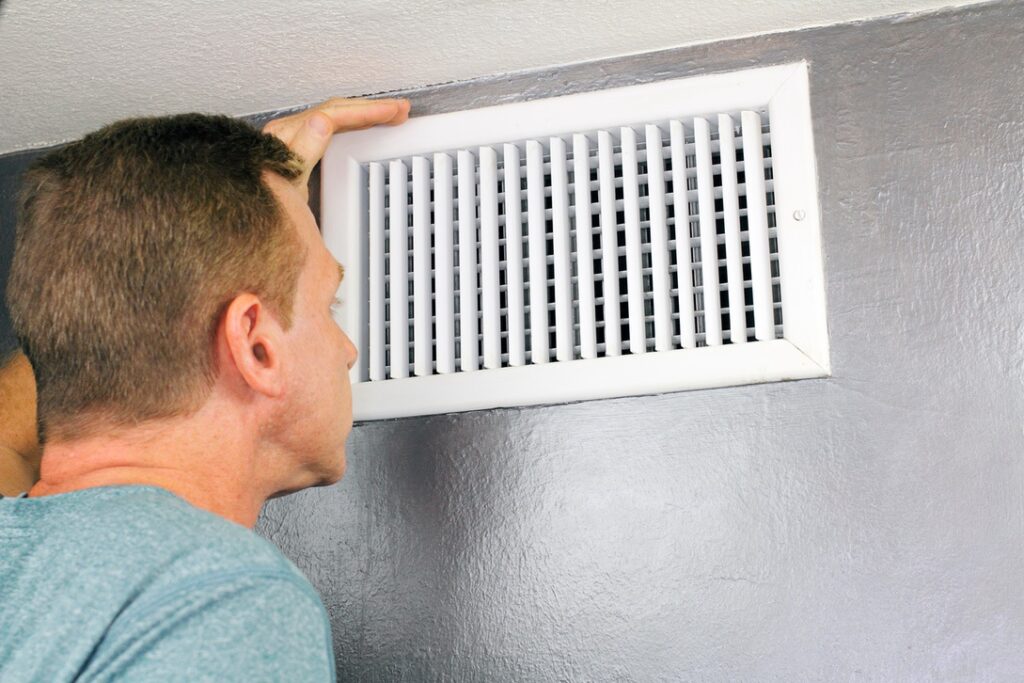 Man inspecting vent in home to determine whether ductwork needs cleaning