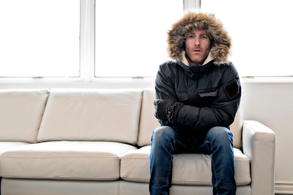 Man shivering on couch wearing winter coat