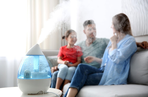 Humidifier running to protect a home's infrastructure in a dry climate with a family sitting on a couch in the background.