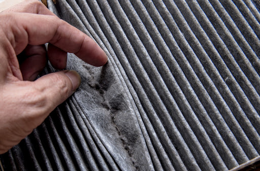 Close up of dirty filter with hand showing dust and debris between filter folds.