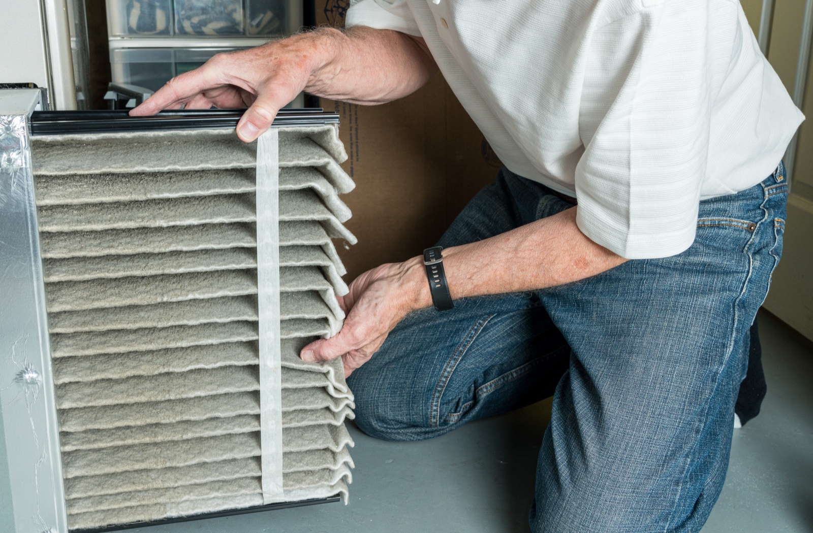 Senior man changing dirty furnace filter from furnace system in his basement.