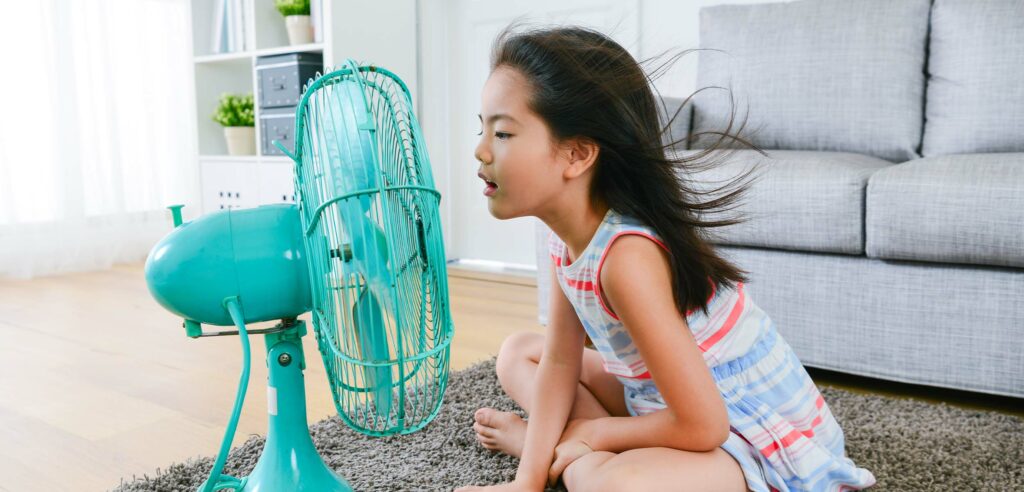 Child cooling themself in front of turquoise oscillating fan.