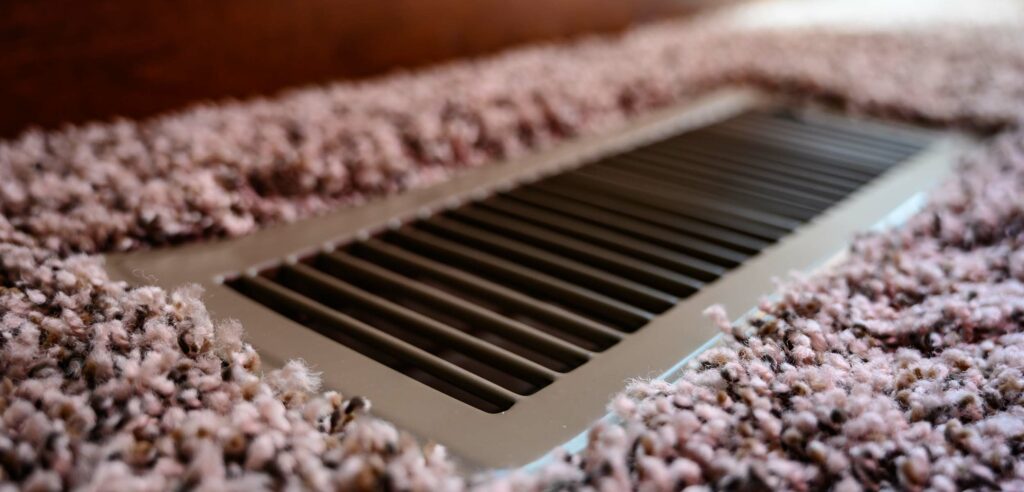 Closeup of heat vent on carpeted floor.