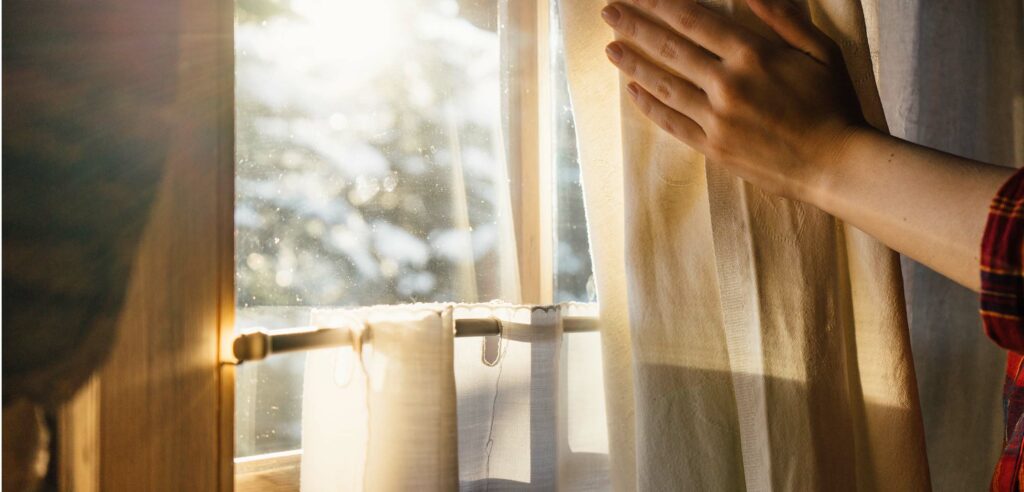 Hand moving living room curtain to reveal light.