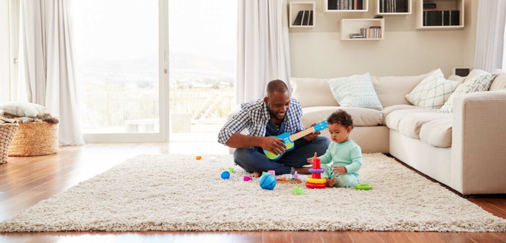 Father and toddler play games on rug in living room.