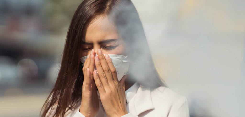 Woman wearing mask and coughing smoky air.