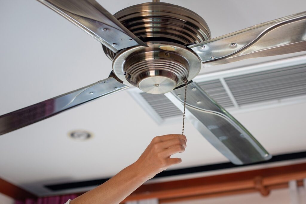 Person reversing direction on ceiling fan to draw cold air upward and improve heating