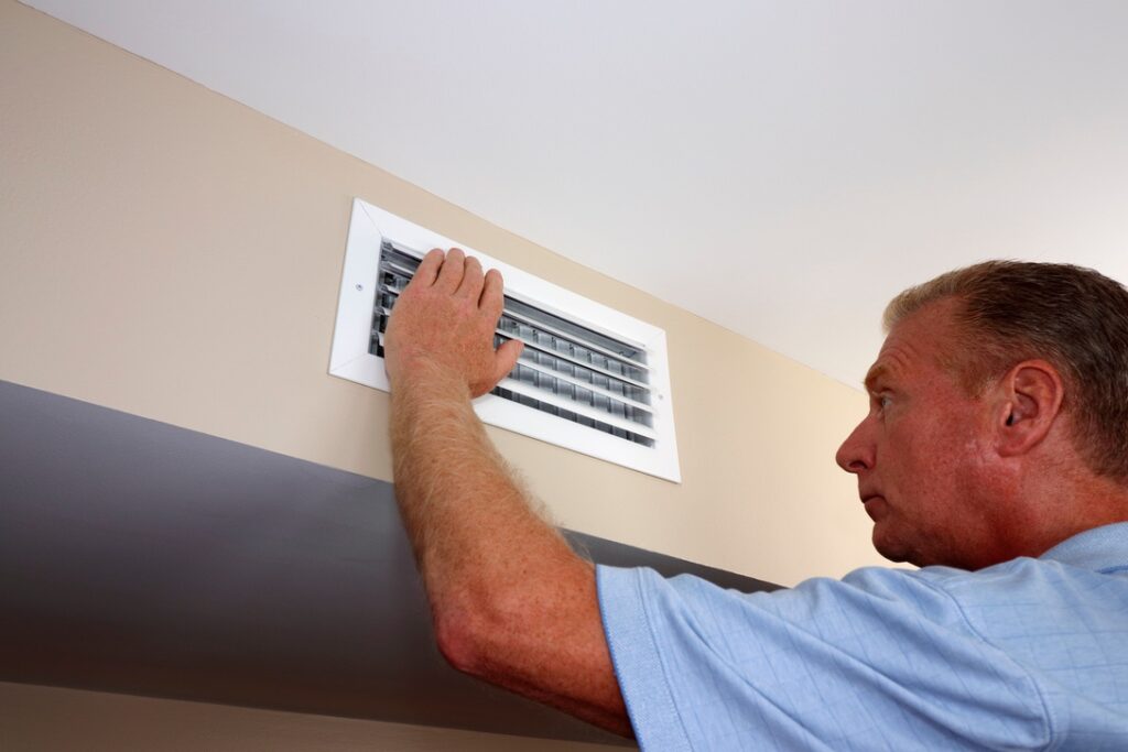 Man checking heat vent in home to make sure it is unblocked
