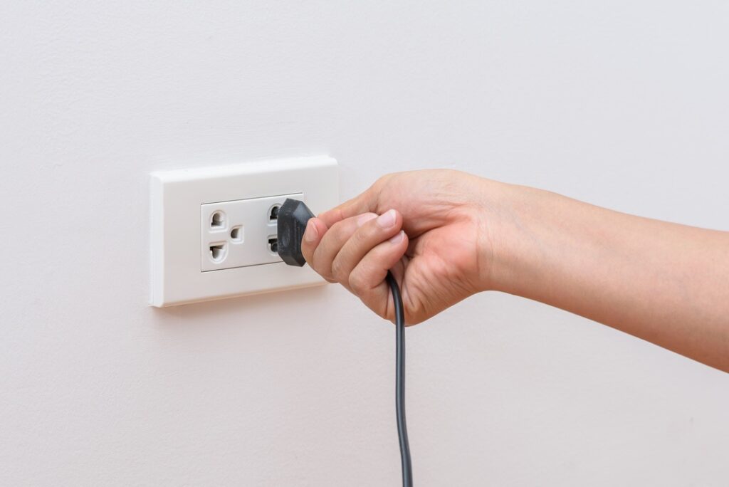 Hand unplugging appliance from wall outlet to reduce heat during Alberta summer