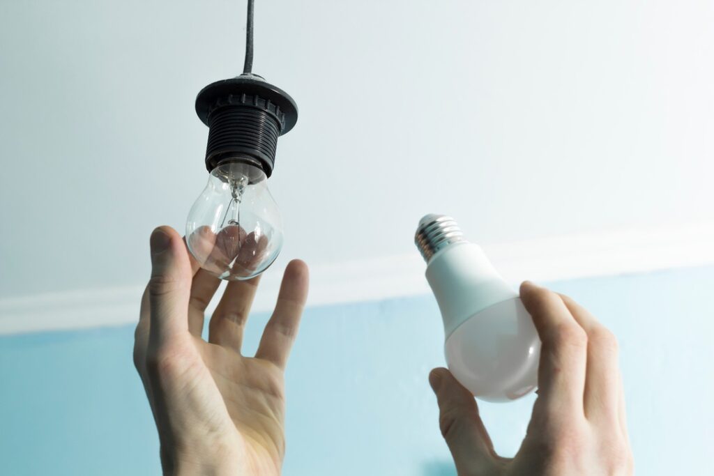 Hand replacing old light bulb with energy efficient new one to reduce heat in home during Alberta summer