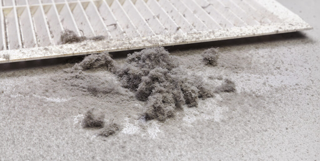 Pile of dust bunnies next to vent grate.