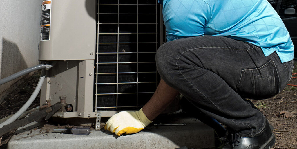 Tech crouching inspecting outdoor AC unit.