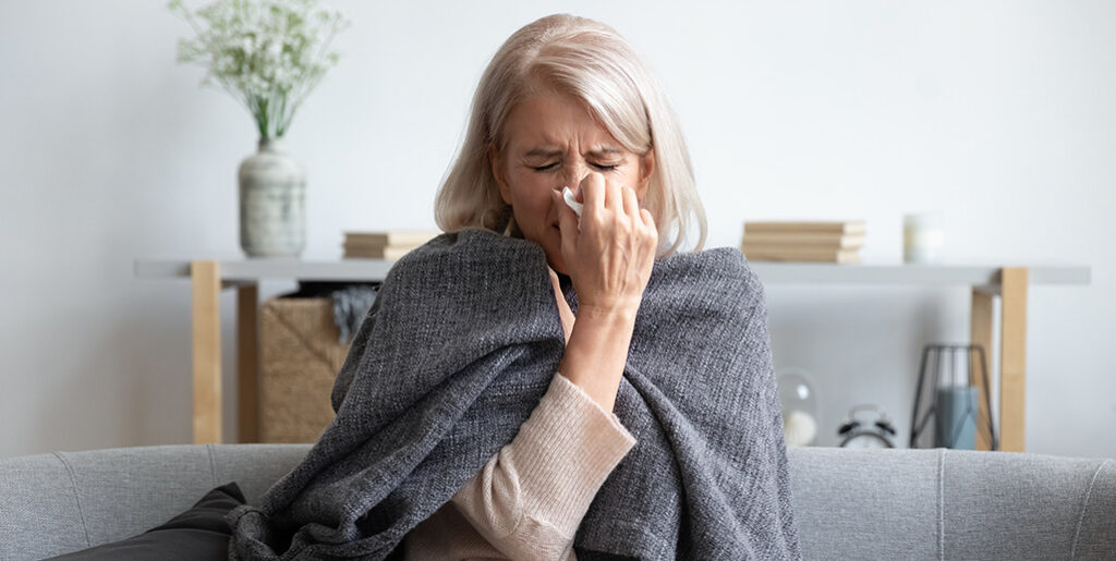 Woman wrapped in blanket blowing her nose.