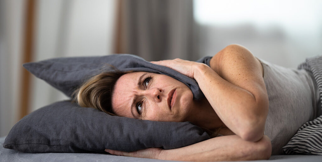 Woman in bed covering ears with pillow