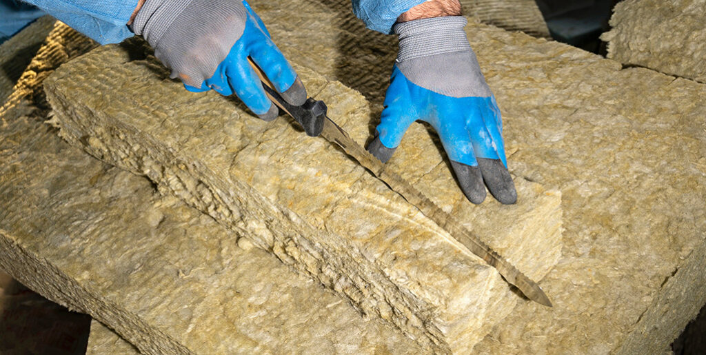 Man wearing gloves cutting fibreglass insulation with long bladed knife