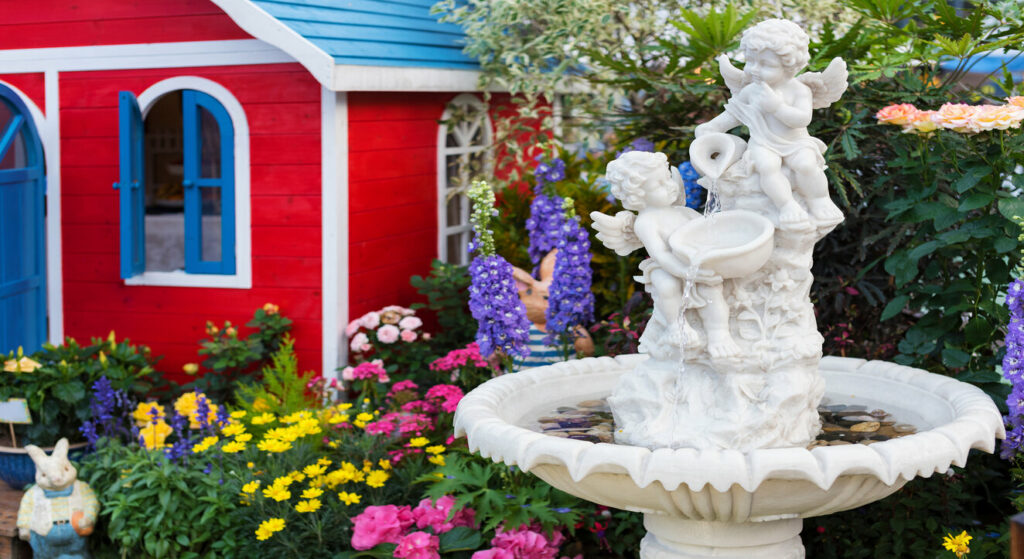 Decorative birdbath surrounded by flowers in front of red guesthouse