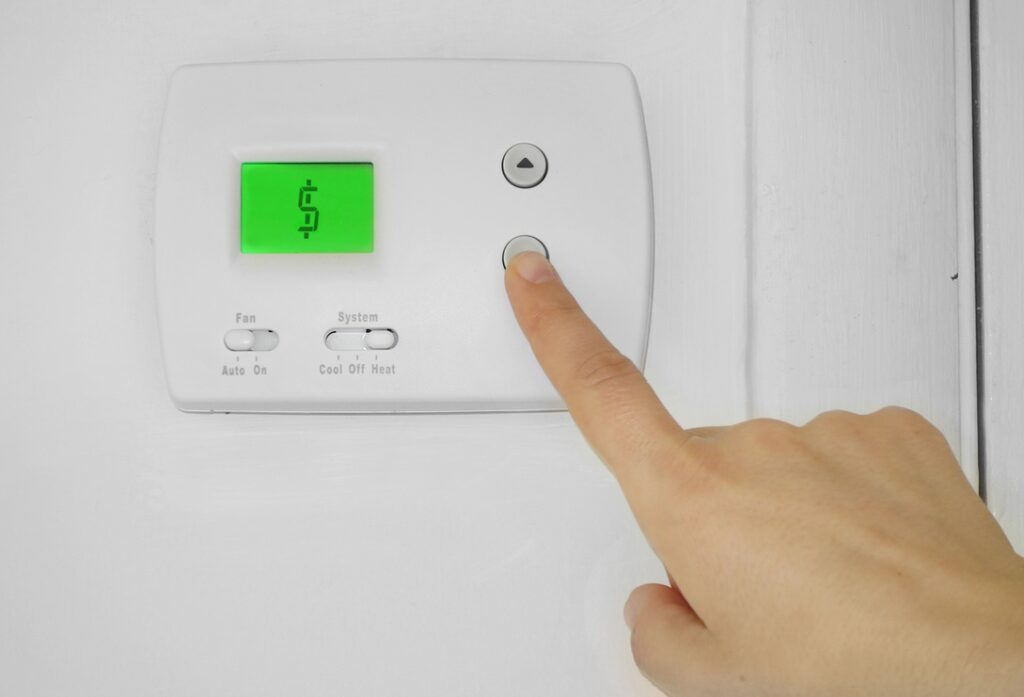 Hand adjusting thermostat with dollar sign on display to symbolize lower bills from new high-efficiency natural gas furnaces