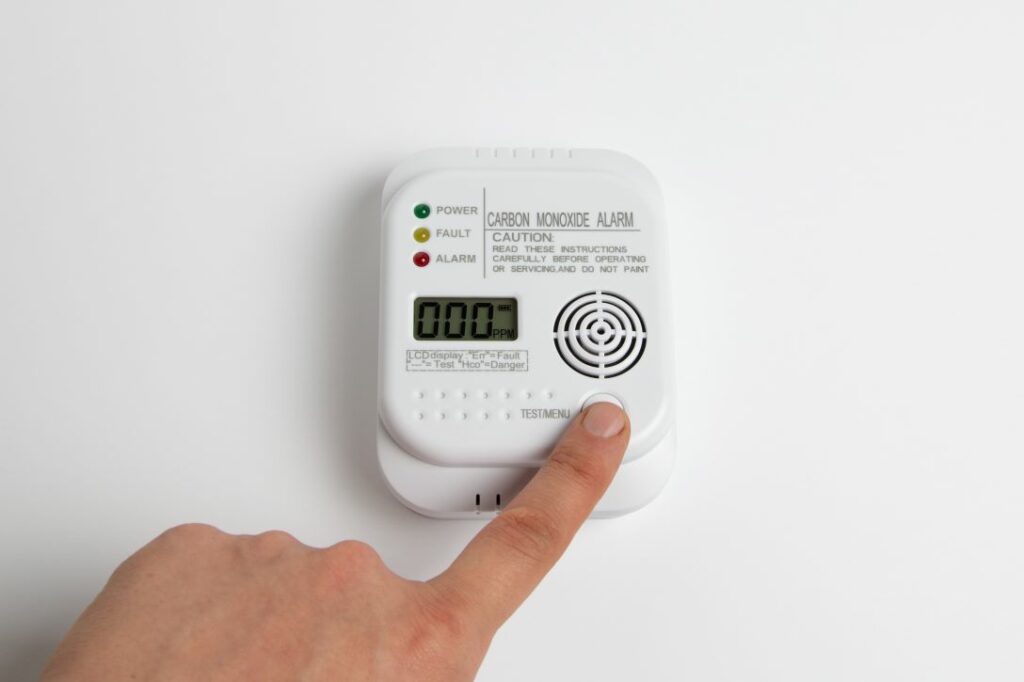 Finger pressing the test button on a carbon monoxide detector