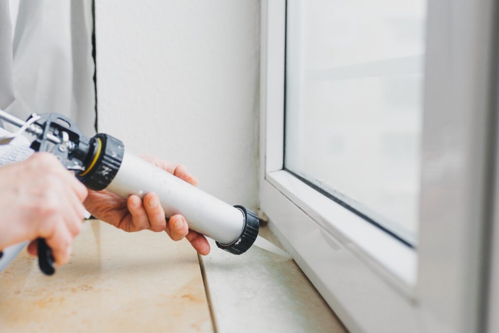 Hands of worker using a silicone tube  for repairing of window indoor