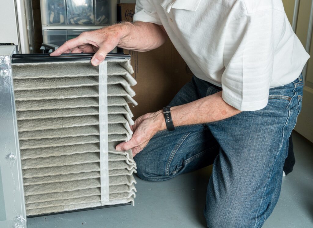Senior caucasian man changing a folded dirty air filter in the HVAC furnace system in basement of home