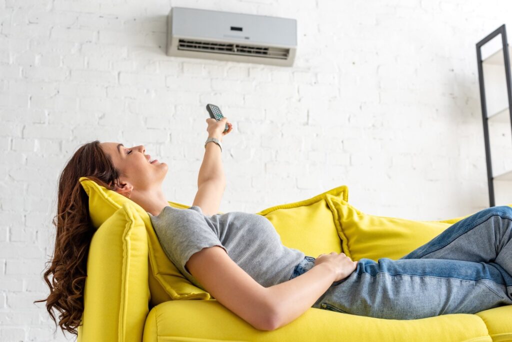 attractive young woman relaxing under air conditioner and holding remote control