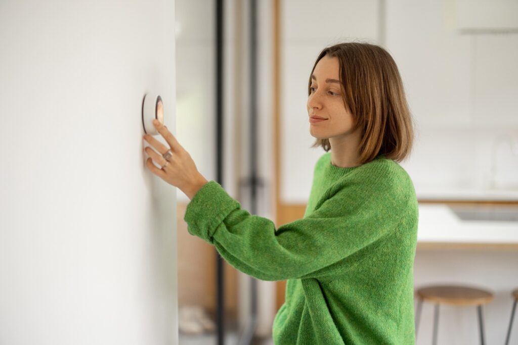 Woman in green sweater adjusting thermostat settings during winter