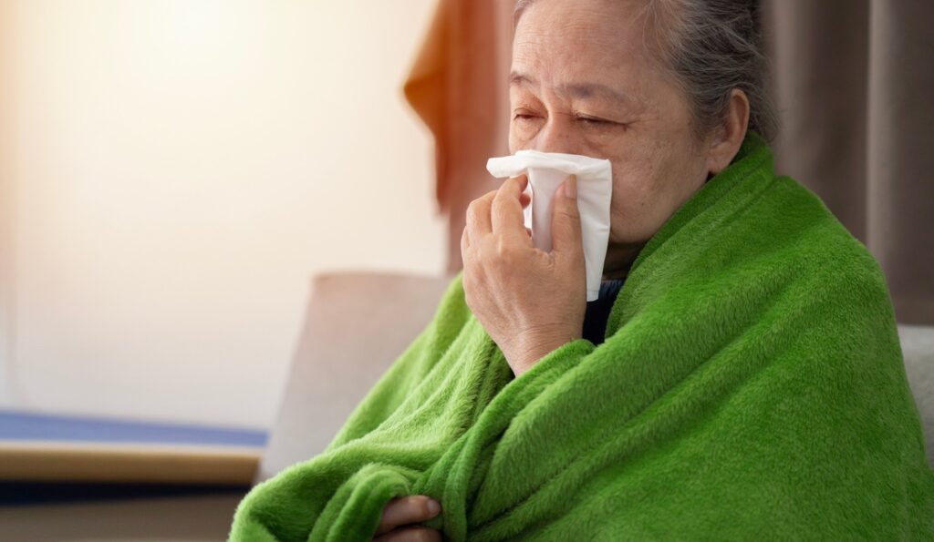 Woman with Sick Building Syndrome holding tissue to face and wearing blanket due to improperly maintained AC unit