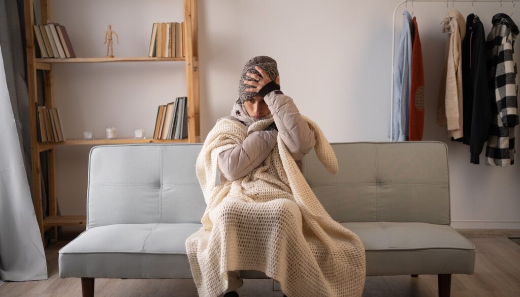 Woman in hat and blankets indoors to represent furnace emergency via uneven or absent heating