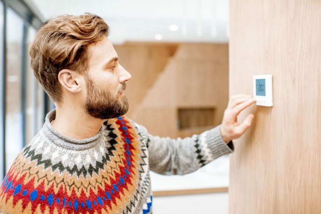 Man using programmable smart thermostat to adjust furnace before leaving home