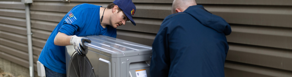 Two Action Furnace technicians carefully install a brand new heat pump at a Calgary home.