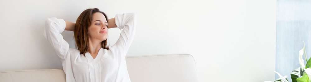 An image of a young woman relaxing on the sofa at home, enjoying the cool and fresh air. The scene conveys the concept of beating the summer heat.