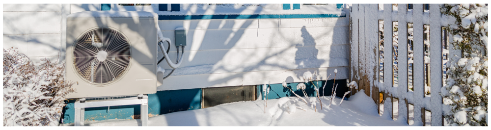 A cold-climate heat pump unit installed on the side of a home, set against a winter backdrop.