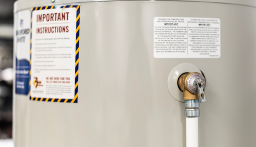 Close-up view of a residential hot water heater tank with safety instruction labels and a pressure relief valve.