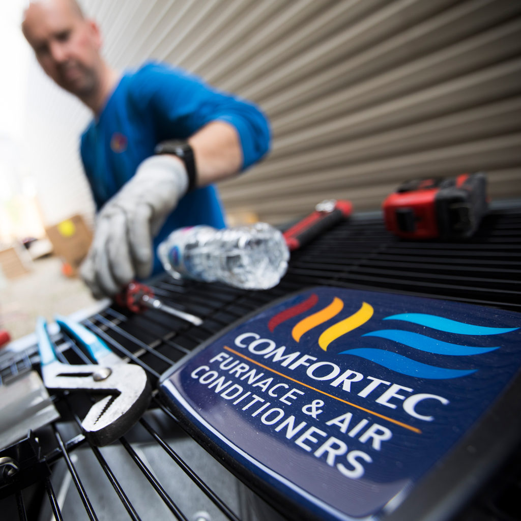 Preparing Your Central Air Conditioner For Winter Worker places wrench and screwdriver atop A/C unit that reads "Comfortec"