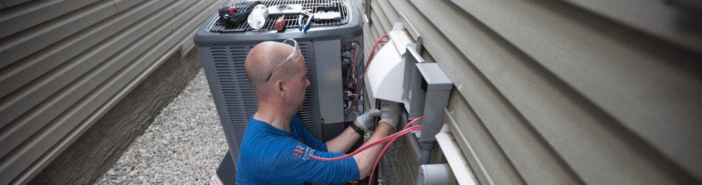 An Action Furnace technician carefully checks the electrical connections on a central air conditioner. Checking electrical components and connections are an integral part of Action Furnace's AC tune-up process.