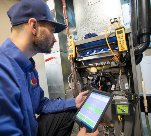 An Action Furnace technician carefully inspects the heat exchanger on a furnace, while his tablet takes readings.