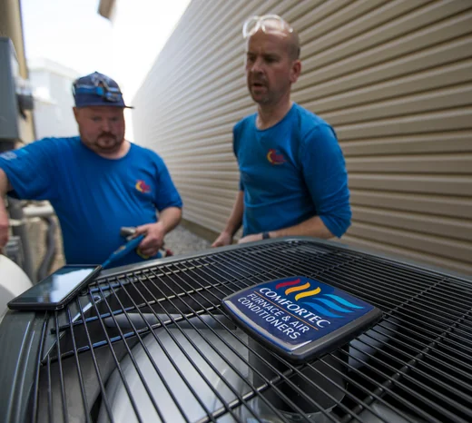 Two Action Furnace technicians inspect an air conditioning unit.