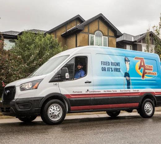 An Action Furnace technician sits in his truck outside a home. He's smiling, indicating a job well done.