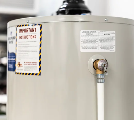 Close-up view of a residential hot water heater tank with safety instruction labels and a pressure relief valve.